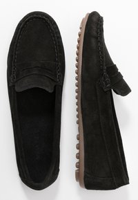 Black suede loafers with a moccasin design, featuring decorative stitching and rubber sole with small circular treads for grip.