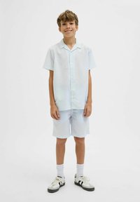 Chemise à boutons bleu clair à manches courtes et short assorti, en tissu texturé, coupe décontractée, portée avec des chaussettes blanches et des baskets noires.