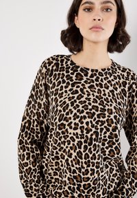 Leopard print sweater in beige with black and brown spots. Long sleeves, round neckline, soft fabric with a ribbed texture.