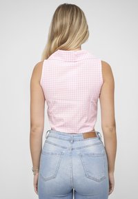 Ærmeløs lyserød gingham-top med krave, kombineret med lyseblå højtaljede denimjeans med lædermærke og baglommer.