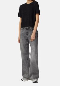 T-shirt noir en tricot coupé associé à un jean en denim gris taille haute et ample. Tissu texturé et détails de couture visibles.