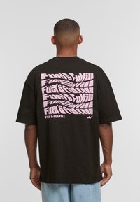 T-shirt in cotone nero con una grande grafica testuale rosa distorta sul retro. Maniche corte e design con vestibilità rilassata.