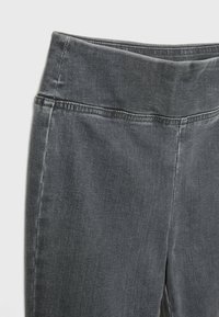 Grijze spijkerbroek met een hoge tailleband, voorzien van subtiele stikseldetails en een gladde textuur. Close-up die de kwaliteit van de stof laat zien.