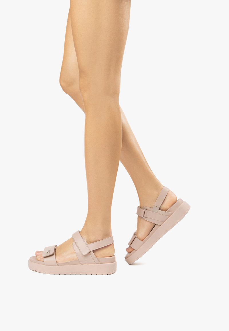 Sandalias de color rosa claro con suela gruesa, correas ajustables y un llamativo detalle de hebilla. Fabricadas con un material sintético suave.