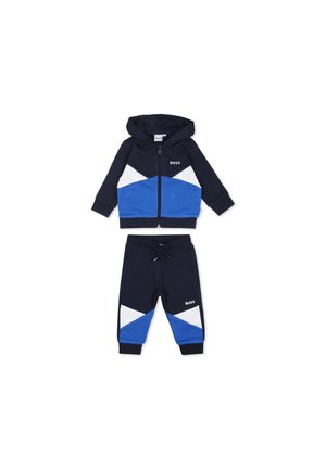 Ensemble de survêtement bleu marine avec des accents géométriques blancs et bleus. Le hoodie présente une fermeture éclair et un logo, tandis que le pantalon a une taille élastique.