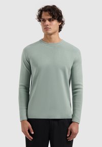 Lichtgroene sweater met lange mouwen en een ronde halslijn, van textuurstof met geribde manchetten, gecombineerd met donkere broeken.