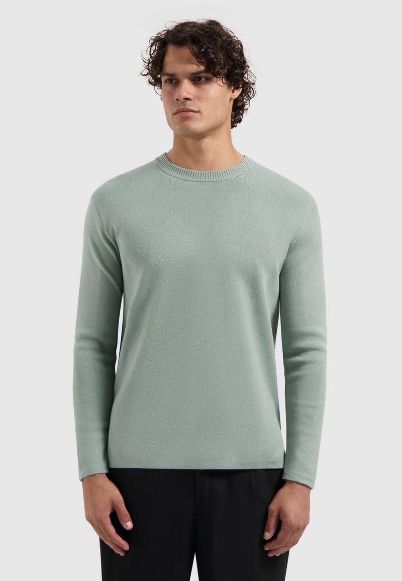 Lichtgroene sweater met lange mouwen en een ronde halslijn, van textuurstof met geribde manchetten, gecombineerd met donkere broeken.