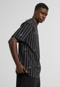 Black short-sleeve T-shirt with white vertical stripes and a repeat pattern of small bird designs. Soft fabric, relaxed fit.