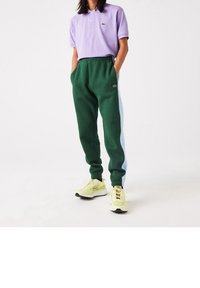 Gröna sweatpants med blå sidopaneler, tillsammans med en lavendelfärgad polo-tshirt. Har en logotyp på både t-shirten och sweatpantsen. Gula sneakers.