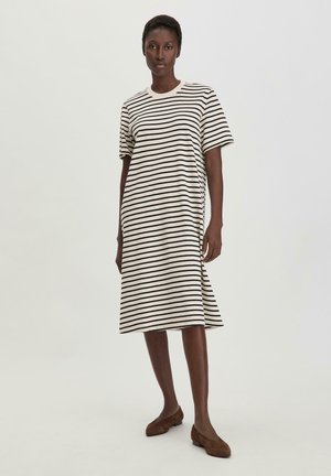 Abito midi a strisce in crema e nero, realizzato in tessuto morbido. Maniche corte e scollo rotondo con vestibilità rilassata. Scarpe flat marroni completano il look.