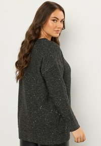 Strickpullover in Dunkelgrau mit metallischen Flecken, mit langen Ärmeln, rundem Halsausschnitt, lockerer Passform und seitlichen Taschen. Texturierte Oberfläche.