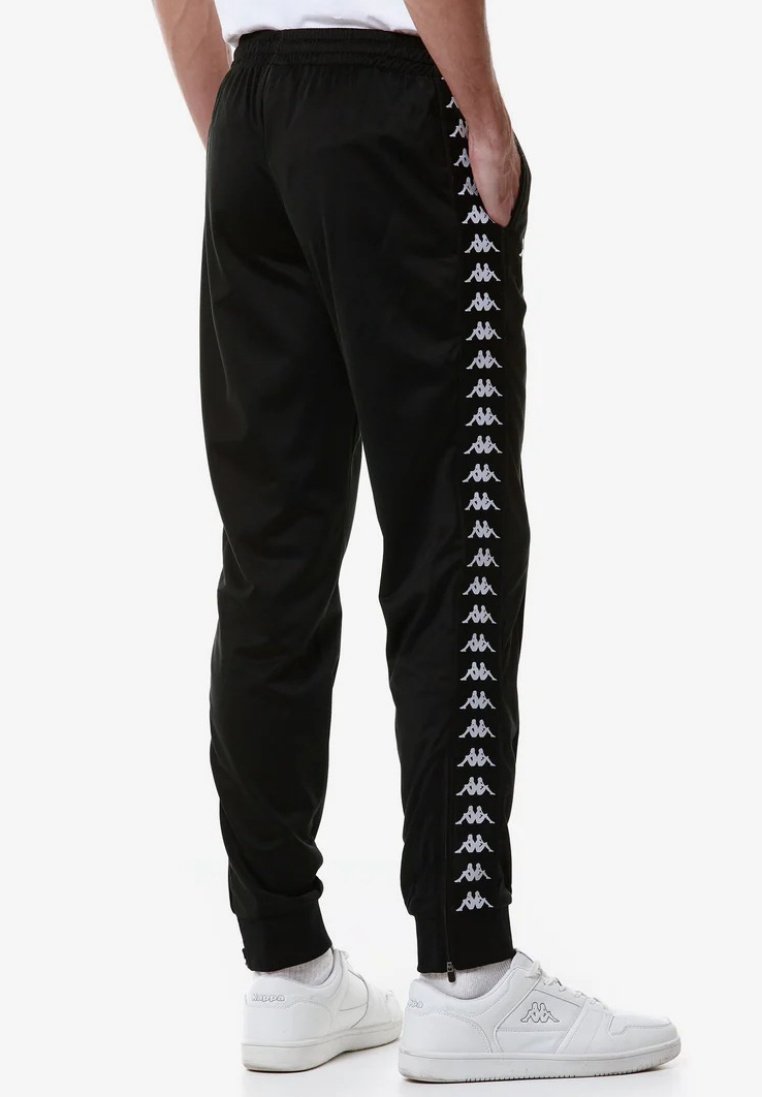 Pantaloni sportivi neri con accenti bianchi lungo i lati, cintura elastica e caviglie affusolate, abbinati a scarpe bianche.