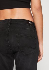Svarta denimjeans med en mid-rise passform, med en logopatch på baksidan och ett unikt sömnadsmönster på bakfickan.