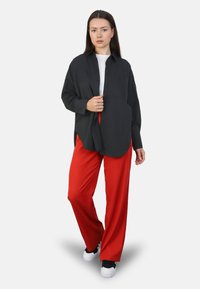 Camisa de botones negra con un corte relajado, mangas largas y bolsillos frontales, combinada con pantalones rojos de pierna ancha y zapatillas negras.