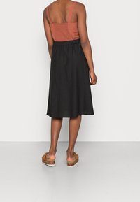 Jupe midi noire avec une taille froncée, associée à un haut ajusté de couleur rouille. La tenue est complétée par des sandales beiges avec un accent en imprimé léopard.