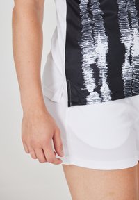 Kortærmet skjorte i sort og hvid med et grafisk mønster, parret med hvide shorts. Glat stof, afslappet pasform, velegnet til aktivt tøj.