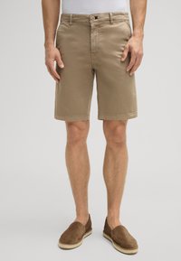 Pantalones cortos de algodón beige de corte recto, con bolsillos laterales y pasadores para cinturón. Combinados con alpargatas de ante marrón.