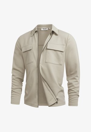 Licht beige jas met ritssluiting, twee borstflapzakken en een klassieke kraag, gedeeltelijk open weergegeven op een witte achtergrond.