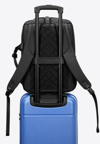 Sac à dos noir avec des bretelles réglables sur une valise rigide bleue présentant des rainures verticales et une poignée télescopique.