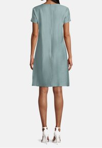 Vestido azul claro hecho de una tela suave, con mangas cortas, corte recto y una costura central en la parte posterior. Combinado con tacones blancos de tiras al tobillo.