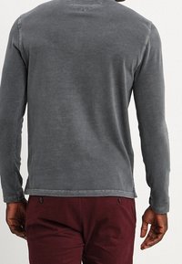 Gray long-sleeve shirt featuring a round neck, a textured finish, and visible stitching accents, paired with burgundy pants.