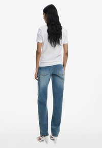 Weißes Kurzarmhemd kombiniert mit lockeren hellblauen Jeans. Die Jeans verfügen über ein klassisches Design mit Gesäßtaschen und einem geraden Schnitt.