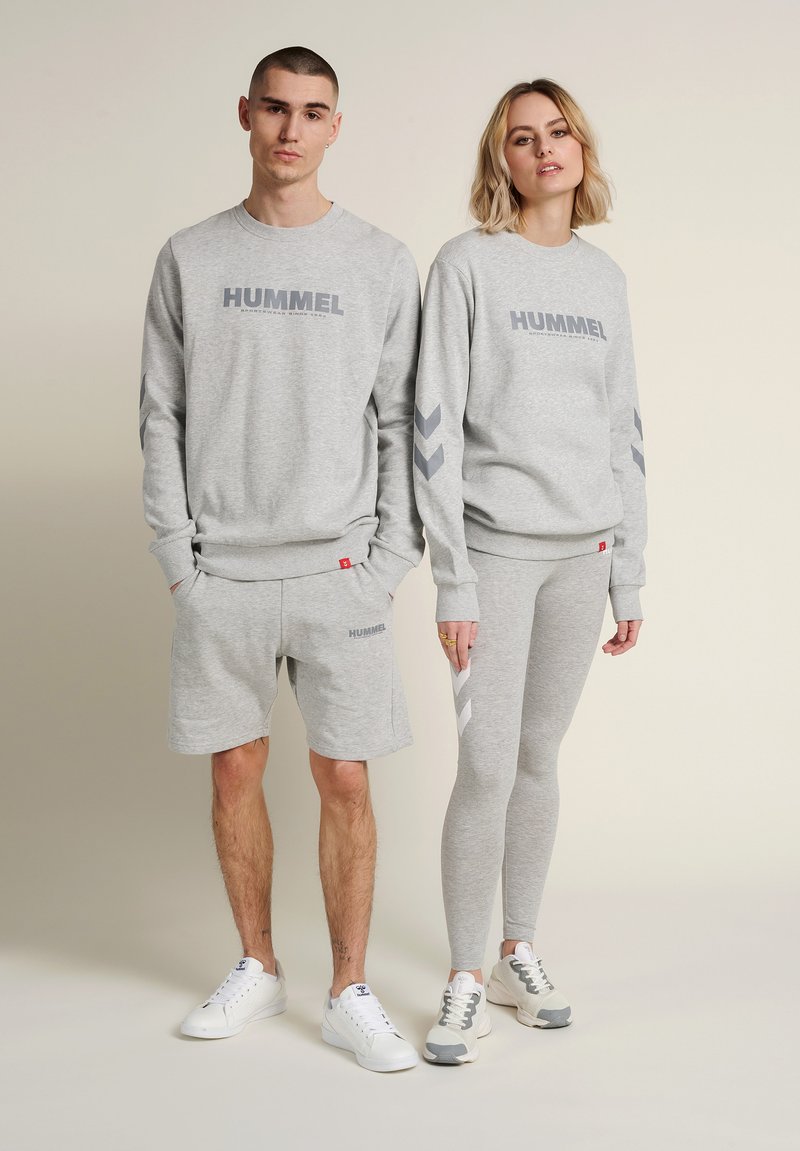 Ung mand og kvinde iført matchende grå Hummel sweatshirts; mand i shorts, kvinde i leggings, begge iført hvide sneakers.