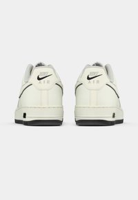 Białe skórzane trampki z teksturowanym szarym językiem, czarnym logo Nike i detalami "AIR" na pięcie. Czarna gumowa podeszwa.