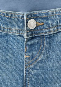 Niebieskie dżinsy z denimu mają srebrne zapięcie na guzik, pomarańczowe szwy i lekko wyblakły kolor. Tkanina ma teksturowany, solidny wygląd.