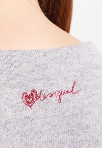 Grauer Strickpullover mit weicher Textur, featuring einem roten gestickten Herzen und einer geschwungenen "lovely"-Akzent auf der Rückseite in der Nähe des Ausschnitts.