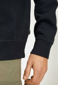 Zwarte sweatshirt met ribgebreide manchetten en zoom, voorzien van een textuurafwerking en een klein labeldetail zichtbaar bij de zijnaad.