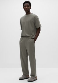 Šedé tričko s krátkými rukávy a volné kalhoty z měkké látky. Mají pohodlný střih a boční kapsy. Šedá obuv na nazouvání.