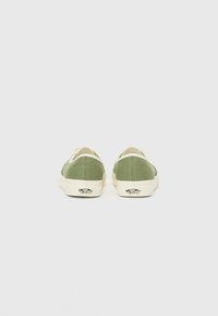 Gröna canvas slip-on skor med en krämfärgad sula, med en logotyp på hälen och ett texturerat tyg för bra grepp.
