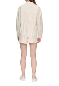 Camisa de botones de rayas color beige claro, de manga larga, combinada con pantalones cortos a juego. El modelo lleva zapatillas blancas con detalles transparentes.