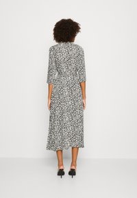 Schwarz-weißes Blumenkleid mit Dreiviertelärmel, taillierter Taille und einem schwingenden Rock, der unterhalb der Waden fällt. Glattes Material, keine sichtbaren Details.