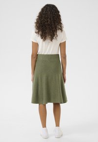 Jupe évasée verte en tissu texturé, taille haute, longueur mi-mollet, associée à un t-shirt blanc et des baskets blanches.