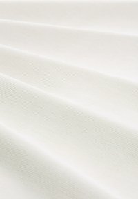 Witte stof met een gestructureerd, geribbeld oppervlak, gerangschikt in plooien, die subtiele variaties in tint en patroon tonen.