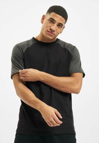 Svart og grå t-skjorte med korte ermer og raglan-design; mykt bomullsstoff; har kontrasterende ermer og rund hals.