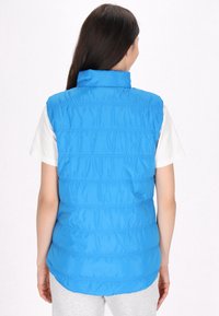 Gilet puffo blu con colletto alto, realizzato in materiale liscio e lucido. Presenta cuciture orizzontali e un orlo posteriore leggermente più lungo.