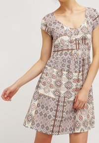 Robe à manches courtes, coupe trapèze, avec un mélange de motifs géométriques et floraux dans des tons de rose, beige et marron. Tissu léger et texturé.