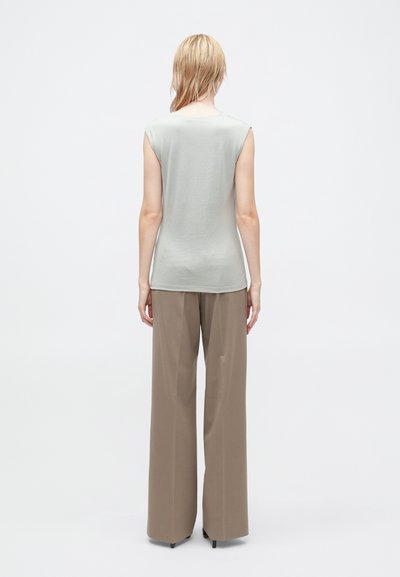 Top senza maniche di un grigio chiaro, con una texture liscia e una vestibilità rilassata, abbinato a pantaloni brown a vita alta e gambe larghe in un tessuto morbido.
