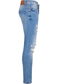 Világoskék skinny farmernadrág, amelyen a combon és a térdnél kopott szakadás található. Egy standard derékpántja és egy barna bőr foltja van a hátsó részen.