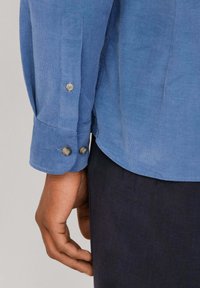 Blauwe corduroy overhemd met knoopmanchetten, heeft een gestructureerde stof, een afgeronde onderkant en twee knopen op elke manchette voor aanpassing.