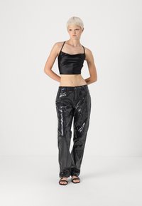 Fekete selyem crop top vékony pántokkal, amelyet magas derekú, csillogó fekete flitteres nadrággal és fekete pántos szandállal kombináltak.
