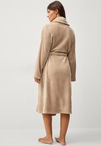 Beige fleece badjas met een sjaalkraag, lange mouwen en een strikceintuur op de taille. Zachte textuur en knielange ontwerp met gestikte zoom.