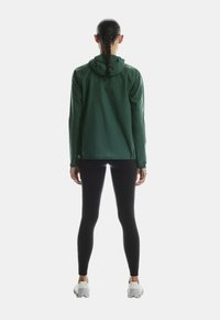 Roheline, kerge jope kapuutsiga, pikad varrukad ja mugav lõige, kombineeritud mustade retuuside ja valgete spordijalatsitega.