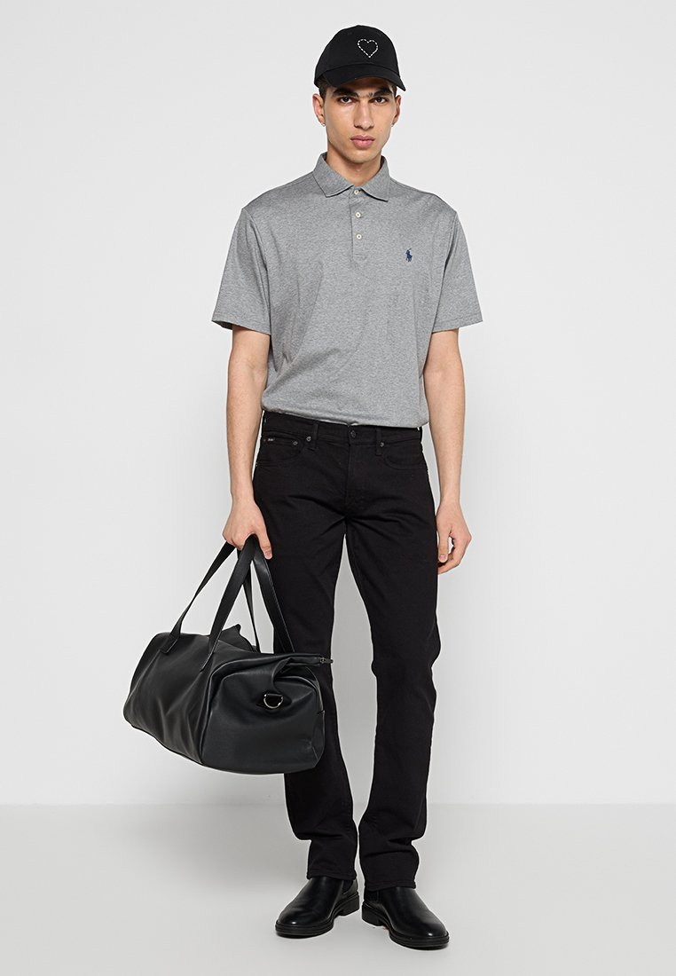 Camisa polo gris con dos botones, combinada con jeans negros. Una gorra negra con un diseño de corazón y una bolsa de viaje de cuero negra. Zapatos negros.