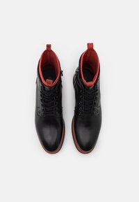 Černé kožené kotníkové boty s červenou podšívkou a červenými gumovými podrážkami. Mezi rysy patří kovové očka a boční zip pro snadný přístup.