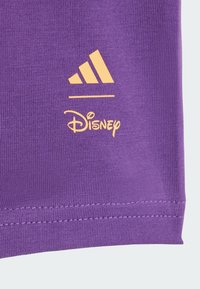 Fioletowa tkanina z wyraźnym żółtym logo Adidas oraz brandingiem Disneya. Gładka faktura z prążkowanymi detalami przy krawędzi.