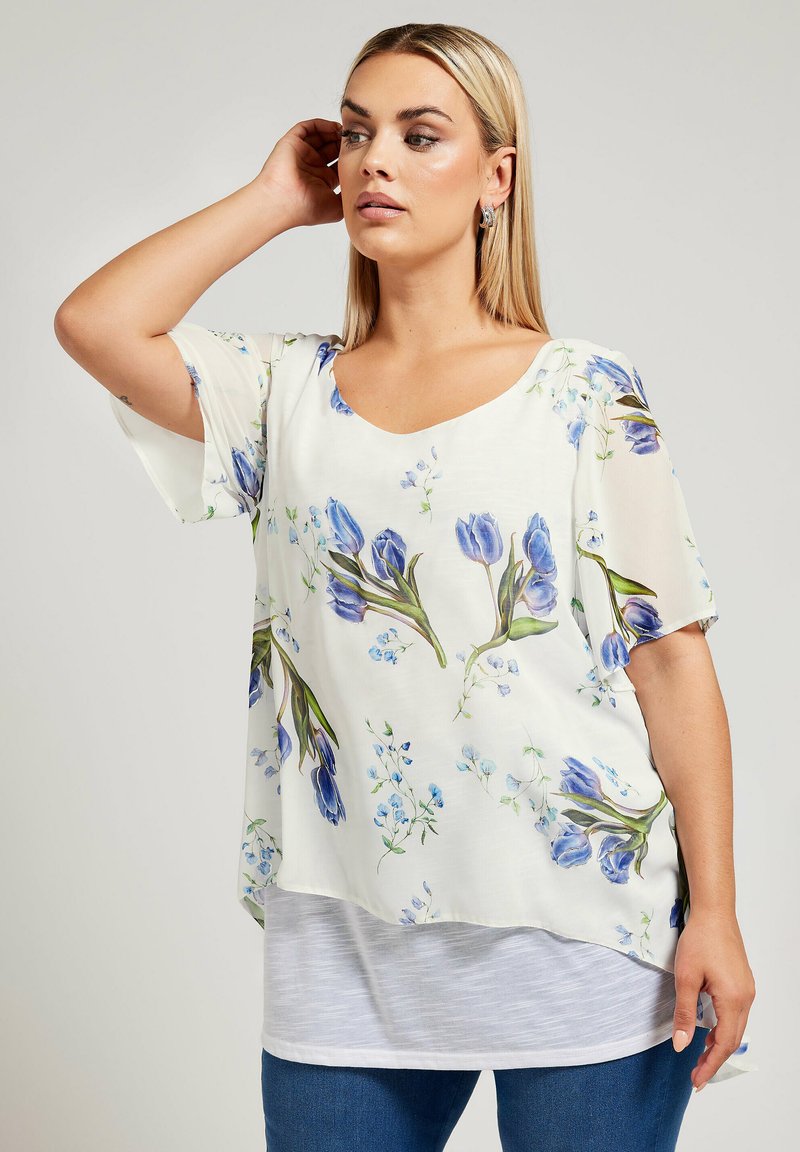 Blusa floreale dal taglio morbido, con motivi di tulipani blu e foglie verdi su uno sfondo cream chiaro. Tessuto morbido e leggero.
